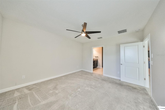 unfurnished bedroom with ceiling fan, ensuite bathroom, light carpet, and a textured ceiling