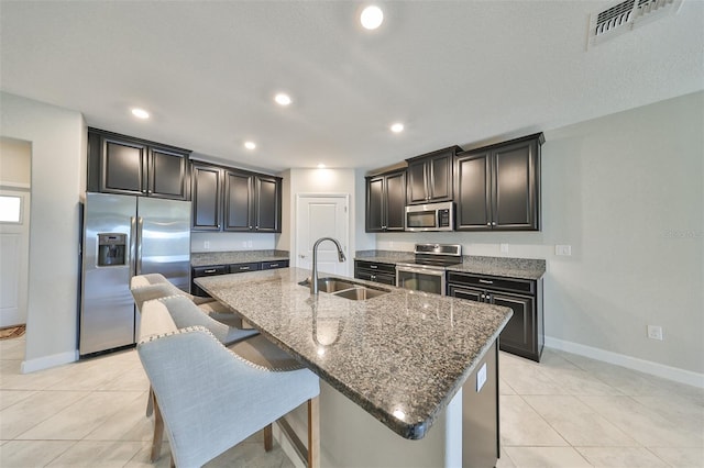 kitchen featuring a breakfast bar area, a center island with sink, stainless steel appliances, dark stone counters, and sink