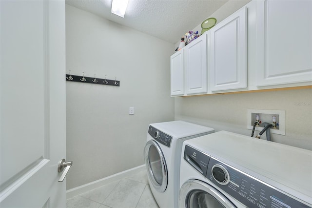 clothes washing area featuring a textured ceiling, cabinets, washing machine and dryer, and light tile patterned flooring