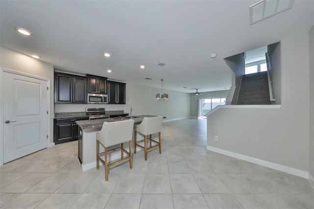 kitchen with decorative light fixtures, stainless steel appliances, a center island with sink, a breakfast bar, and ceiling fan