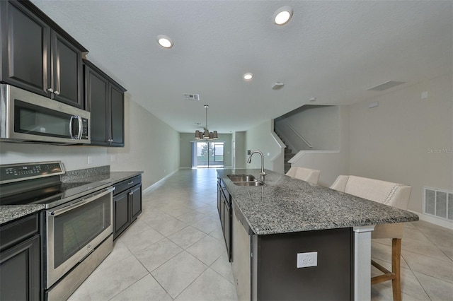 kitchen featuring a breakfast bar, stone countertops, a kitchen island with sink, appliances with stainless steel finishes, and sink