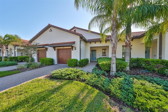 mediterranean / spanish house featuring decorative driveway, an attached garage, and stucco siding