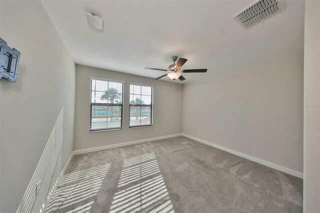 carpeted spare room featuring baseboards, visible vents, and ceiling fan