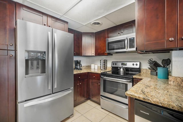 kitchen with a drop ceiling, light stone countertops, stainless steel appliances, and light tile patterned floors