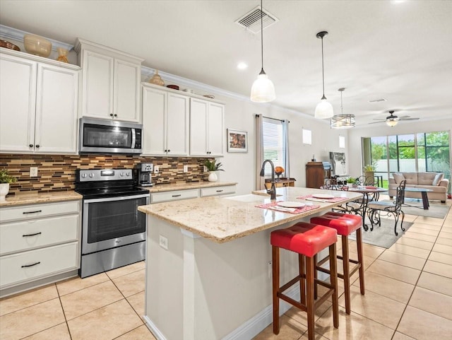 kitchen with ceiling fan, an island with sink, ornamental molding, white cabinetry, and stainless steel appliances