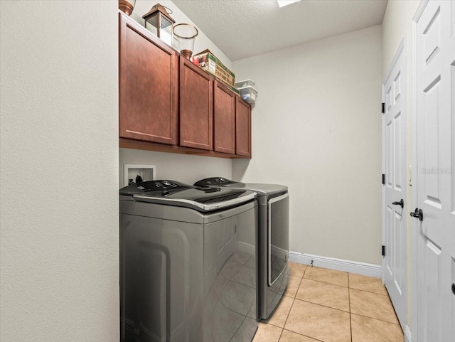 clothes washing area with cabinets, light tile patterned floors, washer and clothes dryer, and a textured ceiling