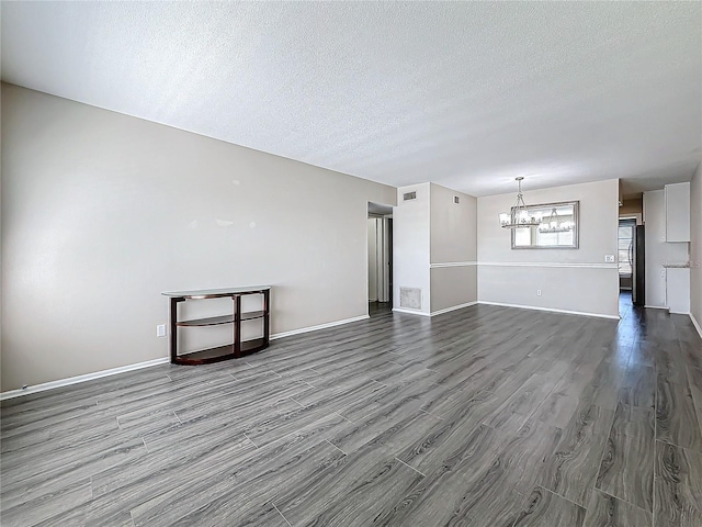 unfurnished living room with an inviting chandelier, a textured ceiling, visible vents, and wood finished floors