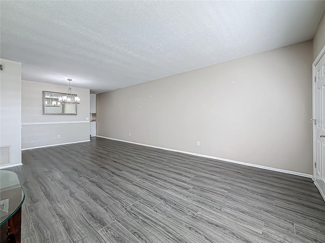 unfurnished living room with visible vents, an inviting chandelier, a textured ceiling, wood finished floors, and baseboards