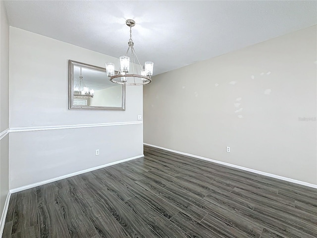 spare room featuring an inviting chandelier, baseboards, and dark wood-type flooring