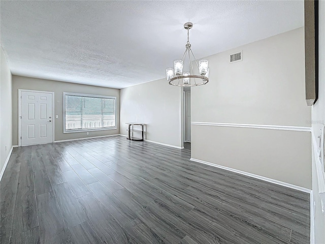 interior space with a textured ceiling, a notable chandelier, dark wood-style flooring, visible vents, and baseboards