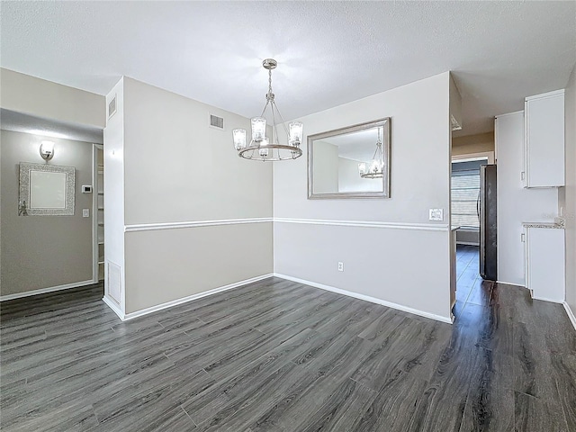 unfurnished dining area featuring a textured ceiling, visible vents, a chandelier, and dark wood-type flooring