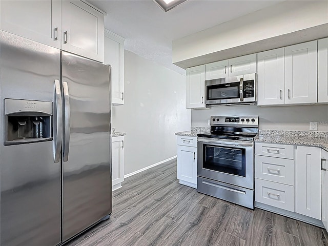 kitchen with light wood finished floors, appliances with stainless steel finishes, white cabinetry, light stone countertops, and baseboards