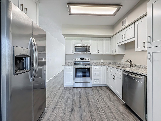 kitchen featuring white cabinets, light stone counters, stainless steel appliances, and a sink