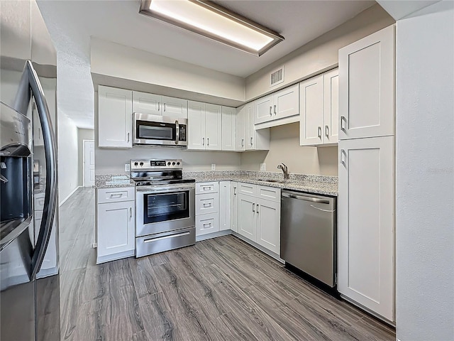 kitchen featuring appliances with stainless steel finishes, white cabinetry, light wood-style flooring, and visible vents