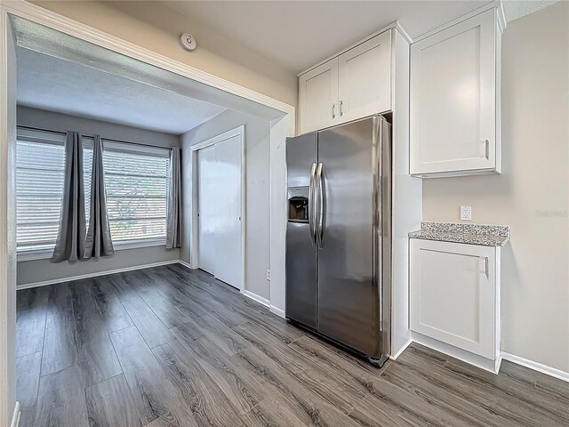 kitchen featuring white cabinets, stainless steel fridge, baseboards, and wood finished floors