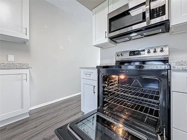 kitchen with a textured ceiling, stainless steel appliances, dark wood-style flooring, baseboards, and white cabinets