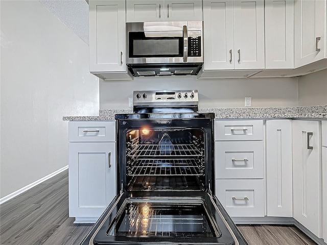 kitchen with electric stove, dark wood finished floors, stainless steel microwave, white cabinetry, and baseboards