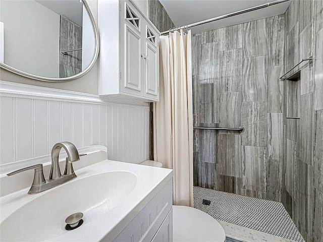 bathroom with wainscoting, a shower stall, toilet, and vanity