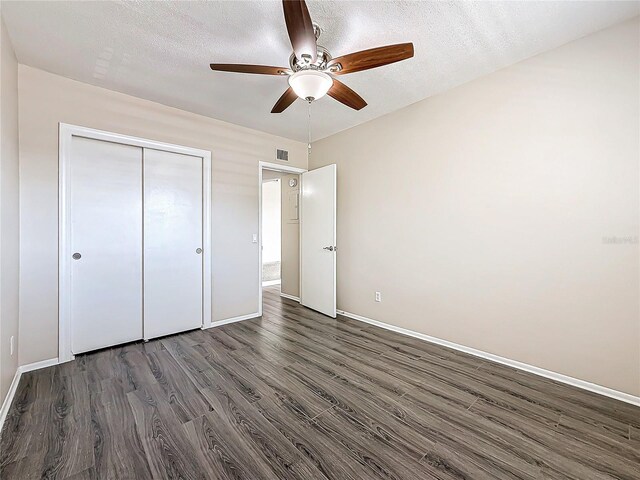 unfurnished bedroom featuring baseboards, visible vents, dark wood-style floors, a textured ceiling, and a closet