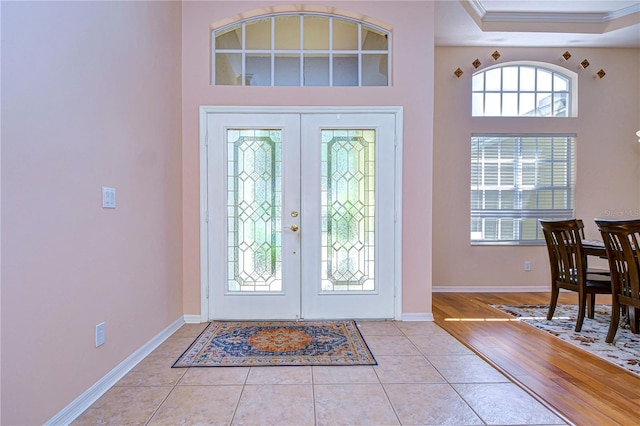 entryway featuring light wood-type flooring, ornamental molding, a tray ceiling, and french doors