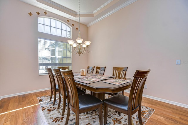 dining room with ornamental molding, an inviting chandelier, a tray ceiling, and light hardwood / wood-style floors