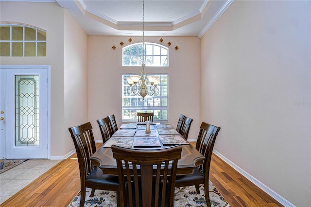 dining space featuring an inviting chandelier, light wood-type flooring, a raised ceiling, and crown molding