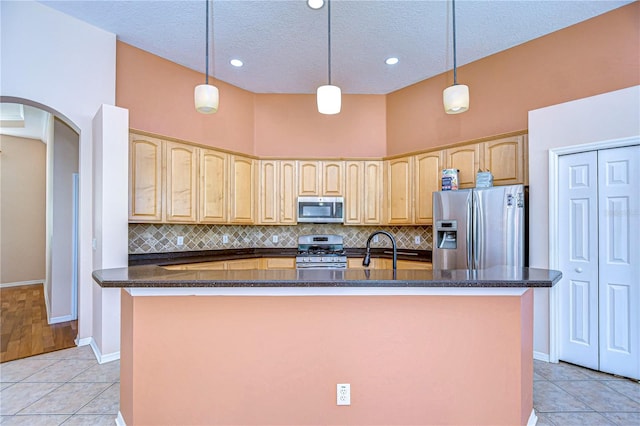 kitchen with appliances with stainless steel finishes, a center island with sink, light tile patterned floors, and decorative light fixtures