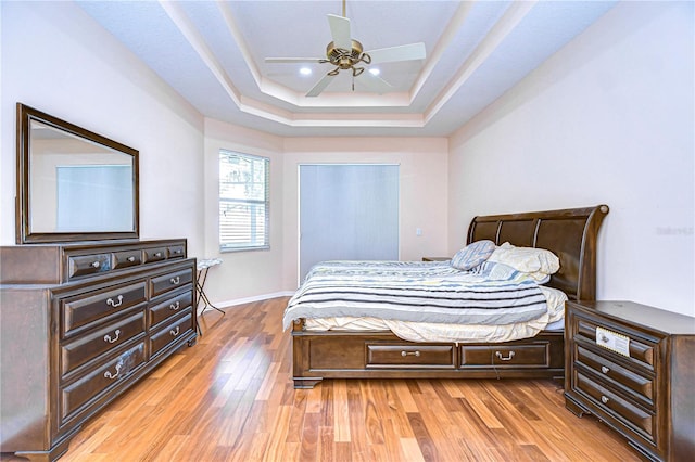 bedroom with light wood-type flooring, a tray ceiling, and ceiling fan