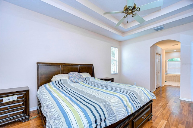 bedroom featuring ceiling fan, light wood-type flooring, ensuite bath, and multiple windows