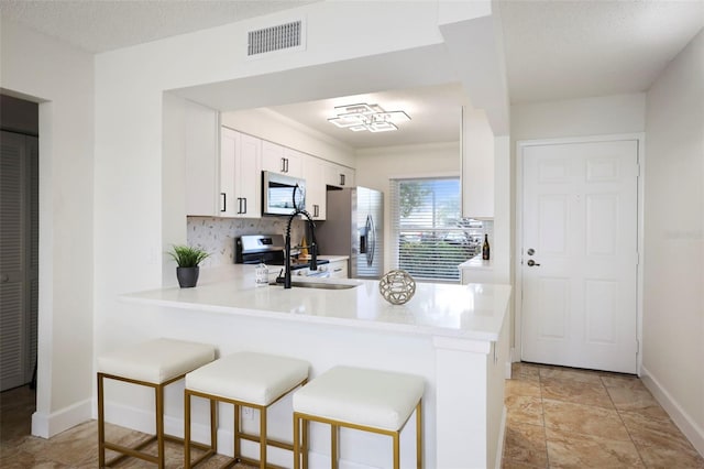 kitchen with kitchen peninsula, white cabinets, a textured ceiling, sink, and stainless steel appliances