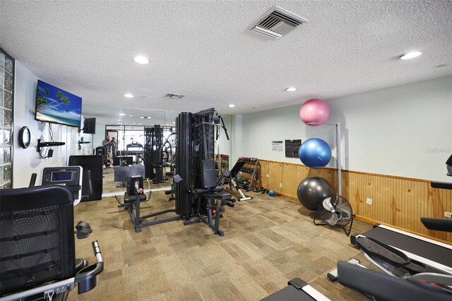 gym with light carpet, wood walls, and a textured ceiling