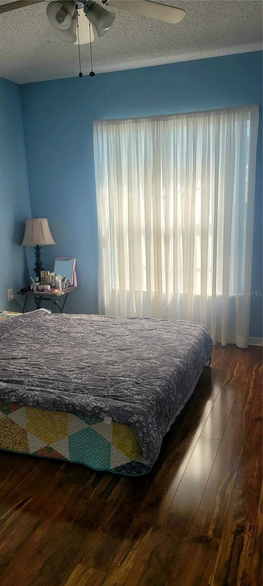 bedroom with ceiling fan, a textured ceiling, and dark hardwood / wood-style flooring