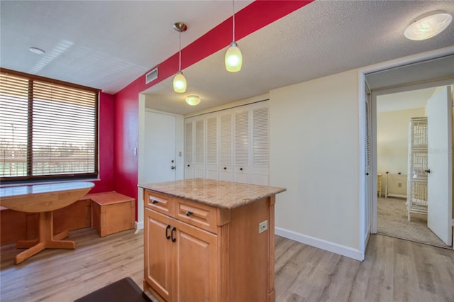 kitchen featuring decorative light fixtures, a textured ceiling, a kitchen island, and light hardwood / wood-style flooring