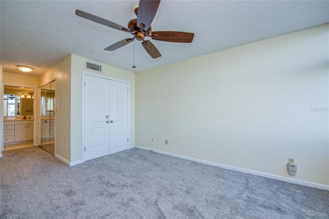 unfurnished bedroom featuring connected bathroom, a textured ceiling, carpet flooring, a closet, and ceiling fan