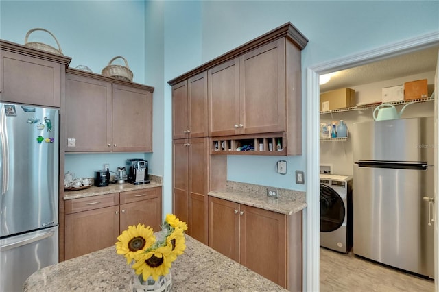 kitchen with stainless steel fridge, washer / clothes dryer, and light stone counters