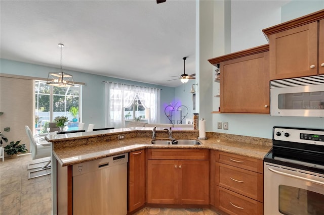 kitchen with light stone counters, sink, ceiling fan with notable chandelier, kitchen peninsula, and stainless steel appliances