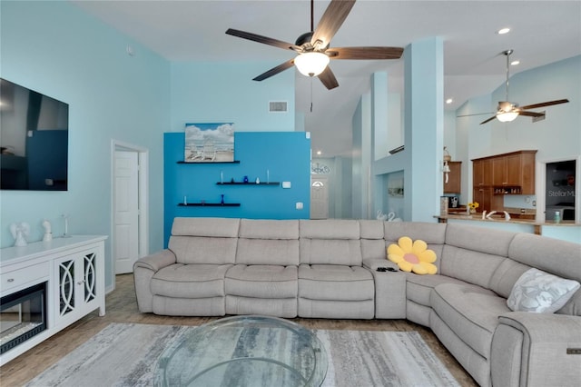 living room with light hardwood / wood-style flooring, a towering ceiling, and ceiling fan