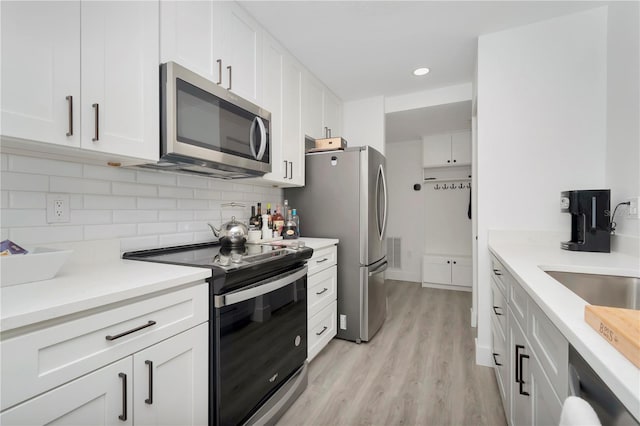 kitchen featuring appliances with stainless steel finishes, decorative backsplash, light hardwood / wood-style floors, white cabinets, and sink