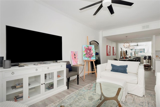 living room featuring light wood-type flooring, ceiling fan with notable chandelier, and ornamental molding