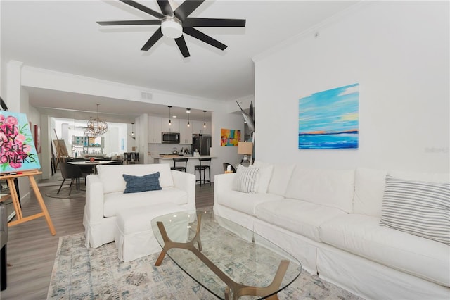 living room featuring ceiling fan with notable chandelier, light wood-type flooring, and ornamental molding