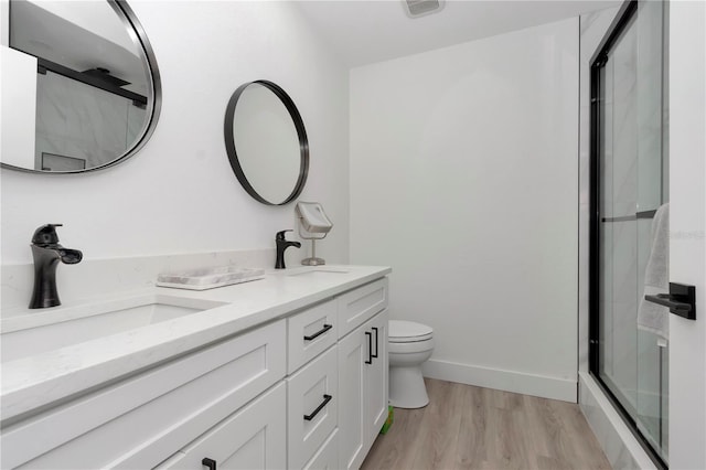 bathroom featuring hardwood / wood-style floors, vanity, toilet, and a shower with shower door