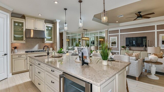 kitchen featuring wine cooler, crown molding, an island with sink, and hanging light fixtures