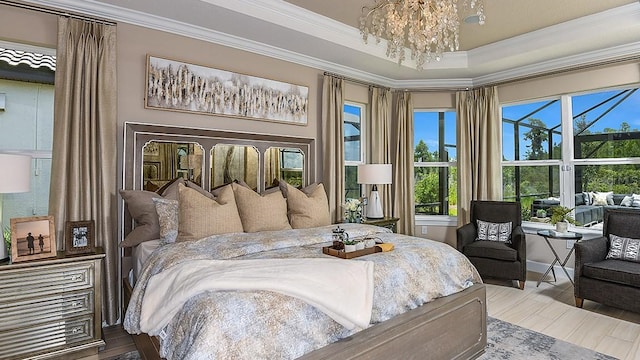 bedroom featuring ornamental molding, wood-type flooring, an inviting chandelier, and a tray ceiling