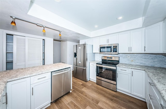 kitchen with appliances with stainless steel finishes, decorative backsplash, light hardwood / wood-style floors, white cabinets, and track lighting