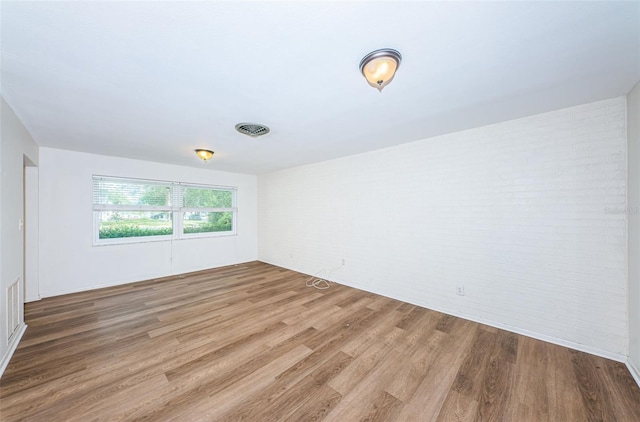 unfurnished room with brick wall and hardwood / wood-style flooring