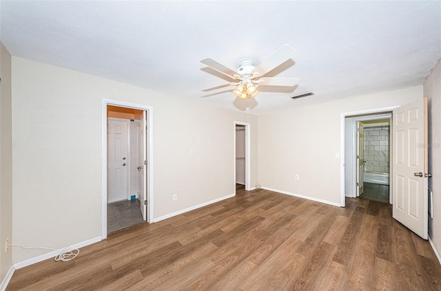 unfurnished bedroom with wood-type flooring, a closet, ensuite bath, a walk in closet, and ceiling fan