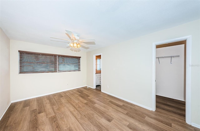 unfurnished bedroom featuring hardwood / wood-style floors, ceiling fan, a walk in closet, and a closet