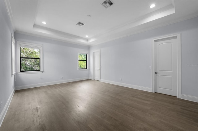 empty room with a raised ceiling, crown molding, and dark wood-type flooring