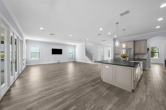 kitchen with dark wood-type flooring, decorative light fixtures, ornamental molding, stainless steel fridge, and an island with sink