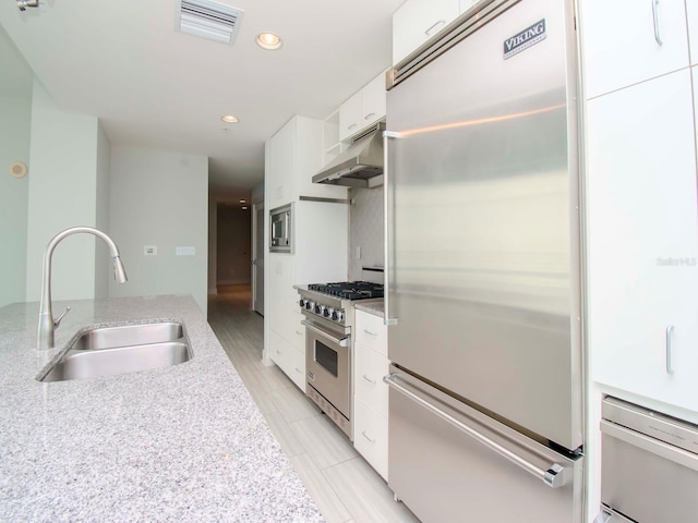 kitchen with light hardwood / wood-style floors, built in appliances, sink, white cabinetry, and light stone countertops